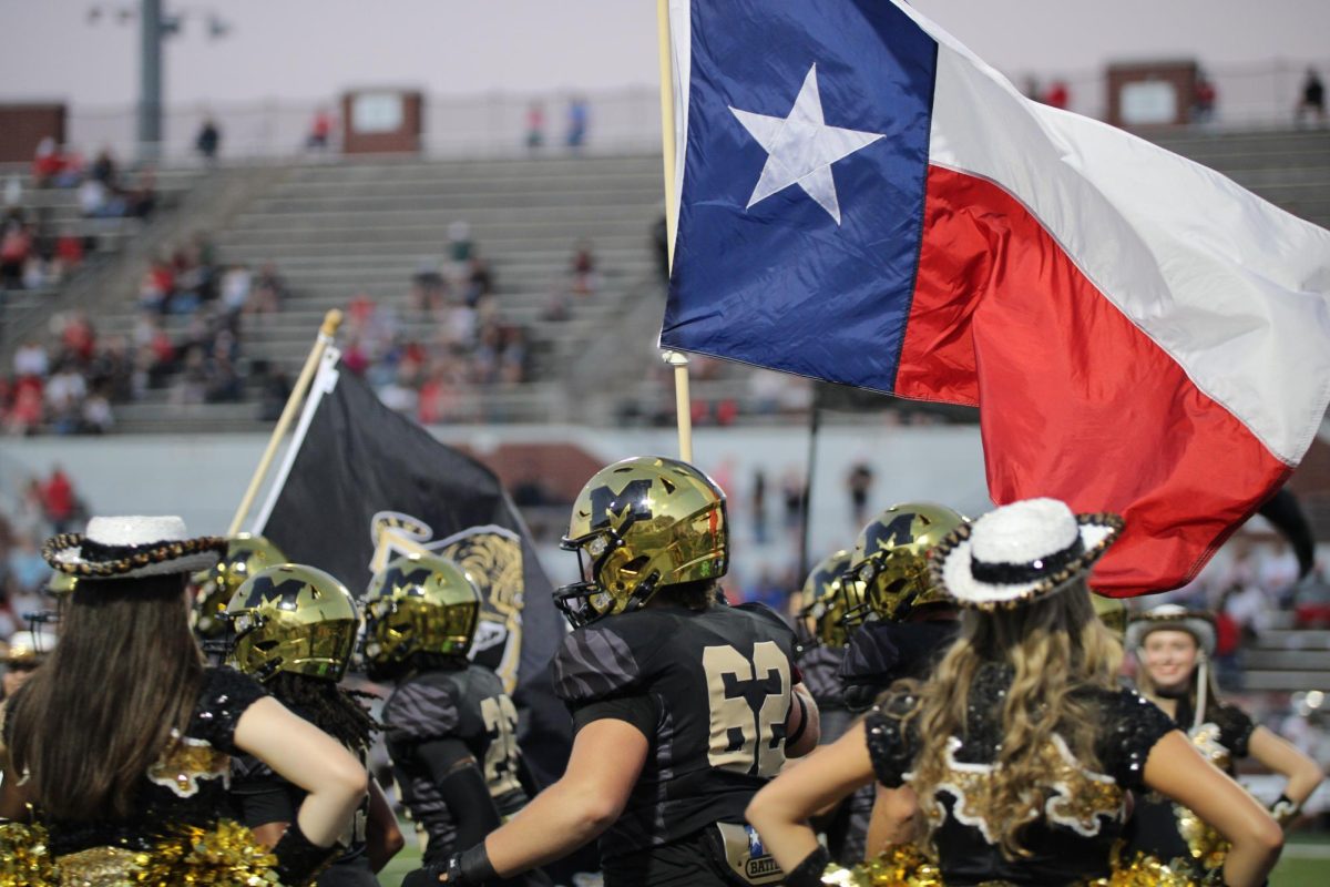 The Football Team carries the Texas flag as they run out.